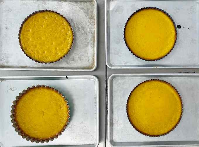 Four lemon tarts baked in tart pans placed on silver baking sheets.